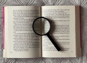 Image shows an open book with a magnifying glass lying on the pages